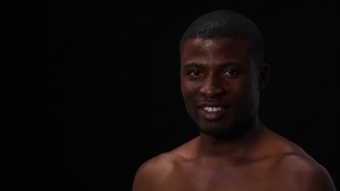 Happy toothy smiling naked black man posing in studio for photographer. Attractive sexy man with short haircut looking at camera over black background.