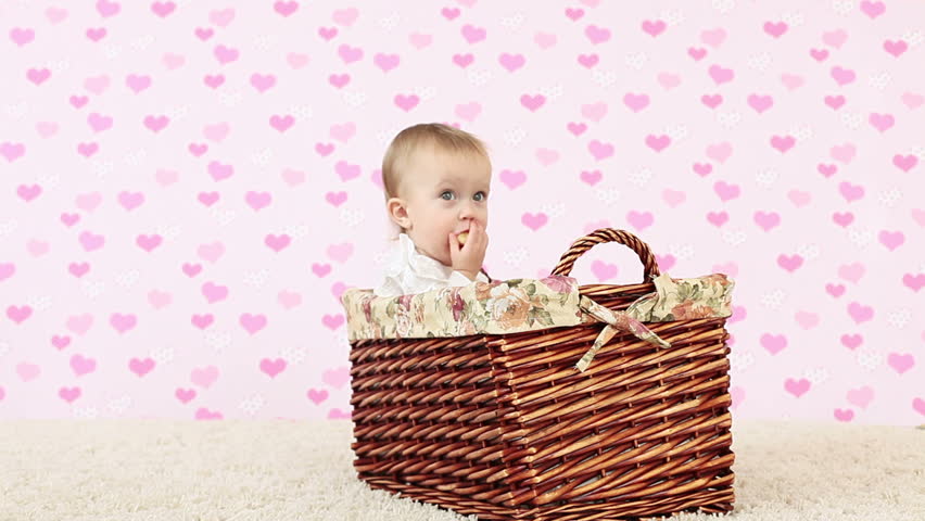 Baby girl eating a banana and sits in a wicker basket