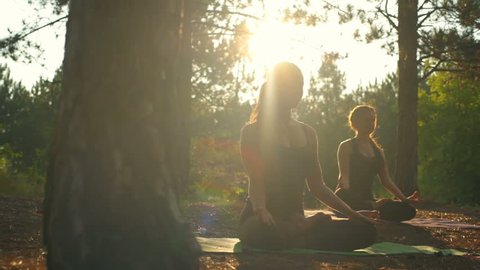 Girls meditating practicing yoga at sunset in forest Padmasana Slow motion