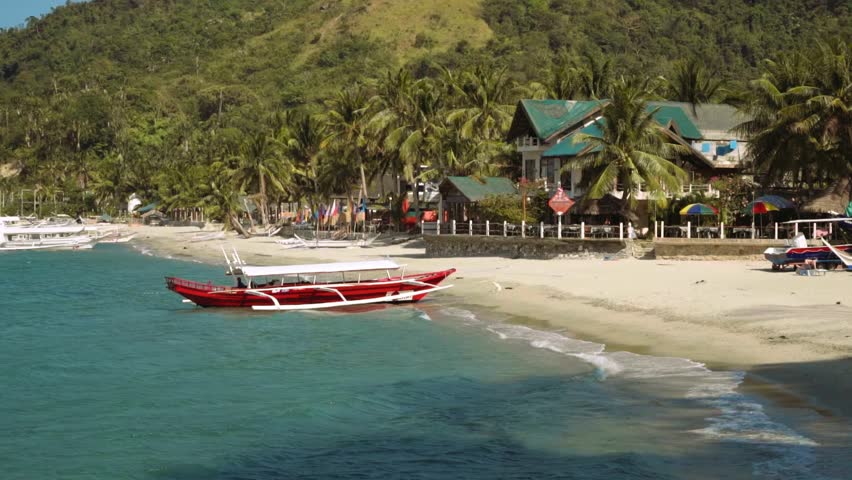 Red outrigger boat on clean white sand beach with a beautiful house, Puerto Galera, Philippines