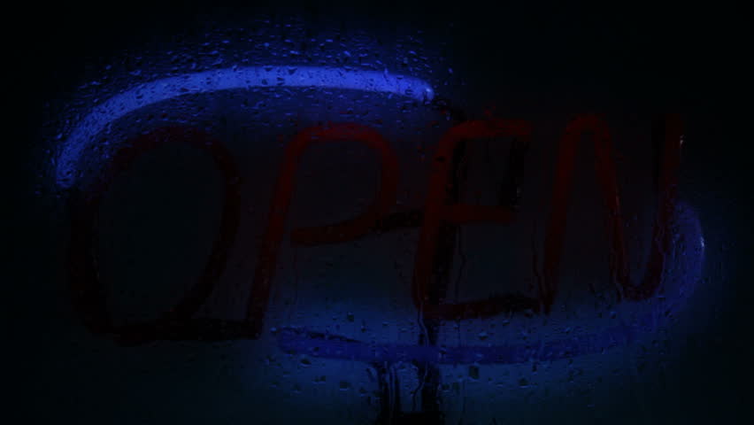 A glowing neon open sign seen through a rain splattered window, with flickering