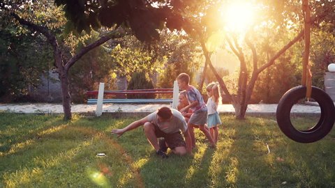 Slowmotion of happy young parents playing with puppy dog and children at park with sunlight shining over small trees and tire swing