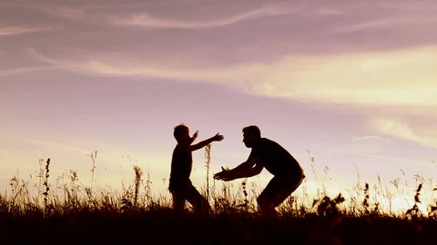 Happy child rushes into hands of father. Family hugs over sunset sky background. Silhouettes of anonymous boy and man outside in summer or autumn landscape. Full hd video portrait of dad and son.