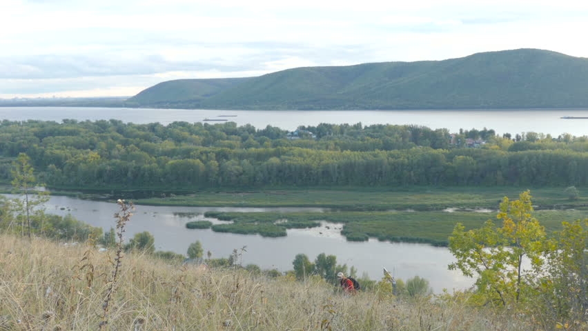 man walking on the hill near the river and enjoying the nature in the sunset.  tourist with a backpack going up the hill to the camera.