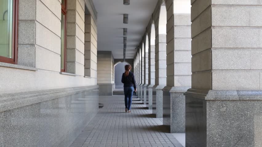 One pretty woman is walking on the long corridor with column.