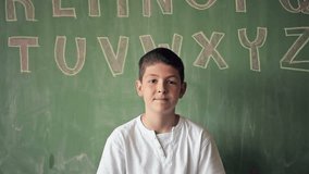 Portrait of a smiling Caucasian schoolboy standing in front of the blackboard. 