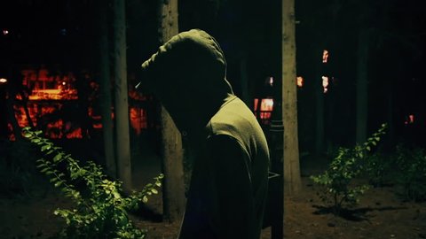 Suspicious hooded figure walks in a dark park at night,100p.A suspicious man wearing a hoodie walks in a dark ominous urban park at night