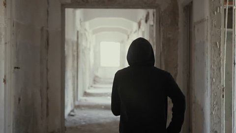 Hooded young man wondering inside destroyed abandoned building,slow motion,dramatic.Millenial with social issues, walks inside a big wrecked empty building in 100fps slow motion.Camera gimbal motion.