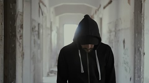 Hooded young man wondering inside destroyed abandoned building,slow motion,dramatic.Young man with social issues, walks inside a big wrecked empty building in 100fps slow motion.Camera gimbal motion.
