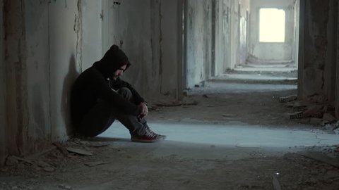 Hooded young man inside destroyed abandoned building,back against wall,slow motion, dramatic.Young man with social issues, inside a big demoloshed building in 100fps.Camera gimbal or crane motion.