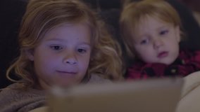 Little Girl Intently Watching Video On Tablet, Her Brother Laughes