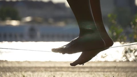 Women's legs balancing on slackline on background sunset water