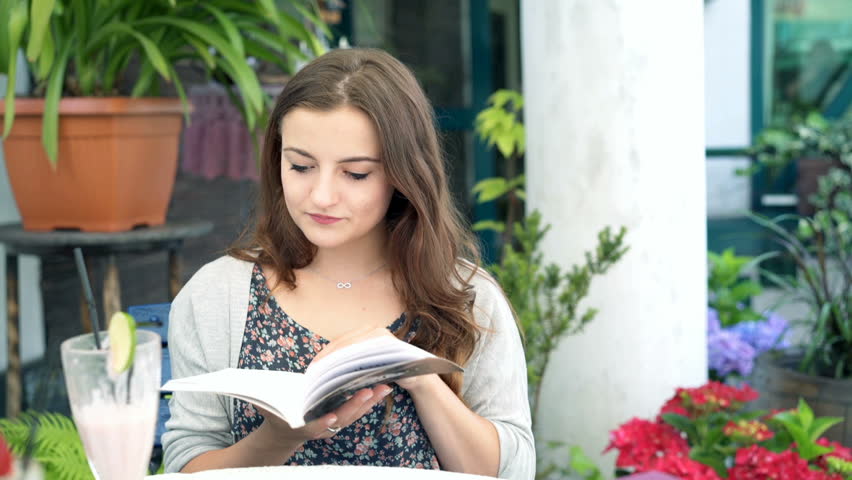 Pretty girl reading book in the cafe and drinking tasty cocktail

