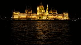 Budapest National Parliament illuminated at night. Danube river in foreground with sailing boats