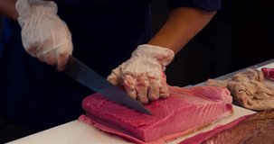 Chef hands cutting with knife raw bluefin tuna to filet pieces 4k video in sushi restaurant kitchen. Asian japanese cuisine.
