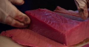 Chef hands cutting with knife raw bluefin tuna to filet pieces 4k close up video in sushi restaurant kitchen. Asian japanese cuisine.