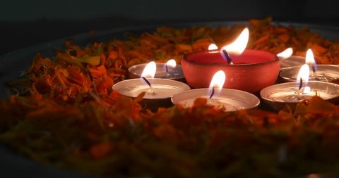 Extreme close up of someone blowing off  Diyas or indian earthen lamp in a silver plate with marigold petals, lit up for Diwali 'Festival of light',surrounded by lit tea-light candles  – Video có sẵn