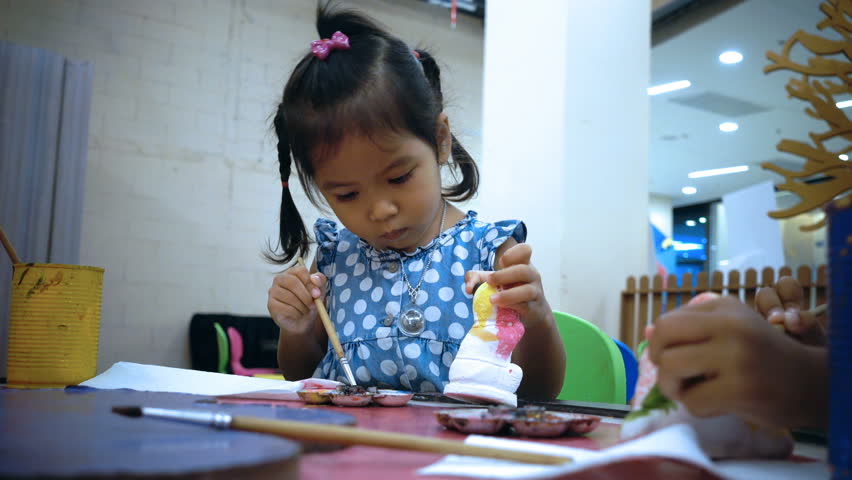 Closeup portrait of little girl learning painting with child hand to white plaster doll toy 