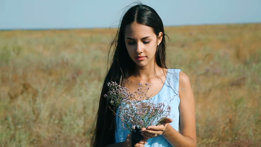 Young beautiful girl in a blue dress enjoys flowers steppe. 