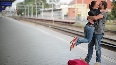 Young couple happy to meet again in the train station, girl runs to meet her boyfriend and throws a suitcase, twist on hands