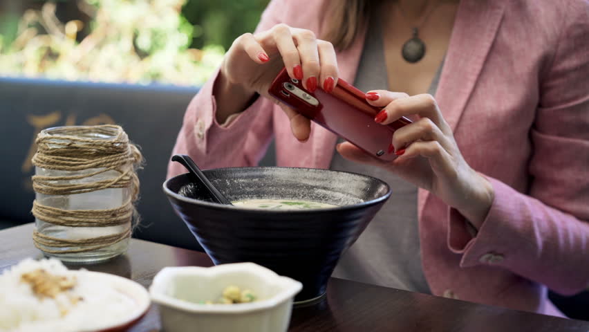 Woman taking photo of soup with cellphone sitting in cafe in garden

