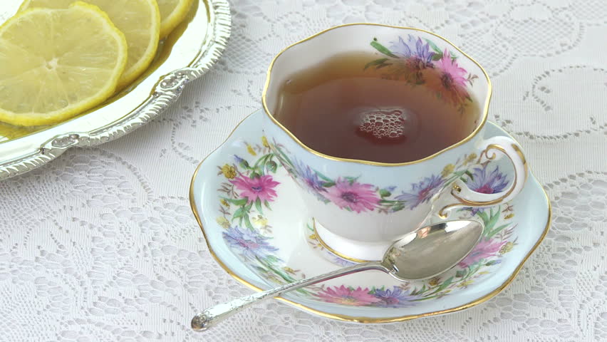 Pouring tea into an antique tea cup, lemons on the side