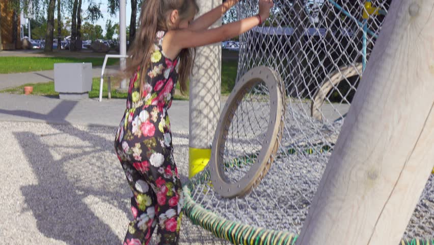 Young girl cilmbs up the net tube on playground, handled camera.