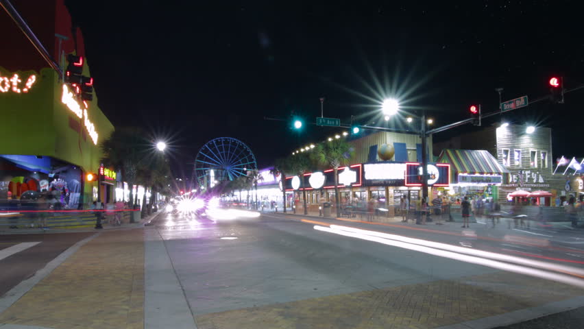 Time lapse of busy Myrtle Beach street corner at night with cars streaking by traffic lights blinking and Ferris wheel in background
