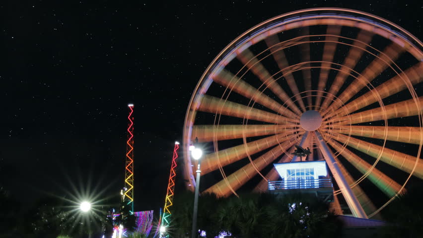 Time lapse pan of ferris wheel at myrtle beach at night with star moving across dark sky