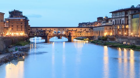 Time lapse of sunset on Ponte Vecchio in Florence, with street lamps light reflections in the water. The "Old Bridge" is a Medieval bridge over the Arno River in Florence, Tuscany - Italy