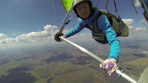 Young woman controls her glider and fly under the cloud base rushing to the finish line on the hang gliding competitions