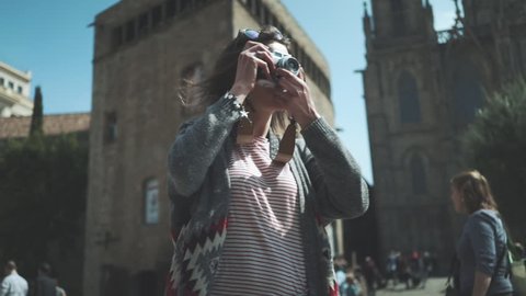 Portrait shot of young hipster traveler girl walking in the city and take picture via vintage camera outside, attractive woman traveling at Europe looking landmarks in Barcelona, slow motion