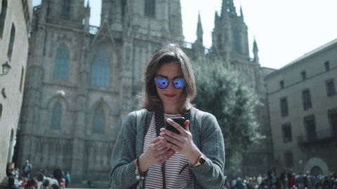 Young hipster traveler girl walking in the city and take picture via smartphone outside, attractive woman traveling at Europe looking landmarks in Barcelona, slow motion