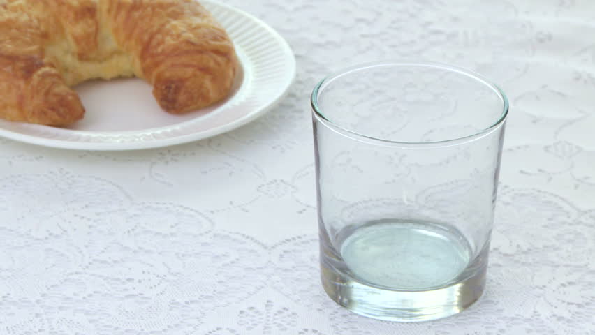 Breakfast Orange Juice being poured into a glass with croissant in the