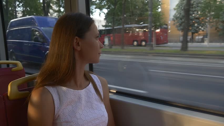 Young woman in white dress looks out the window of tram