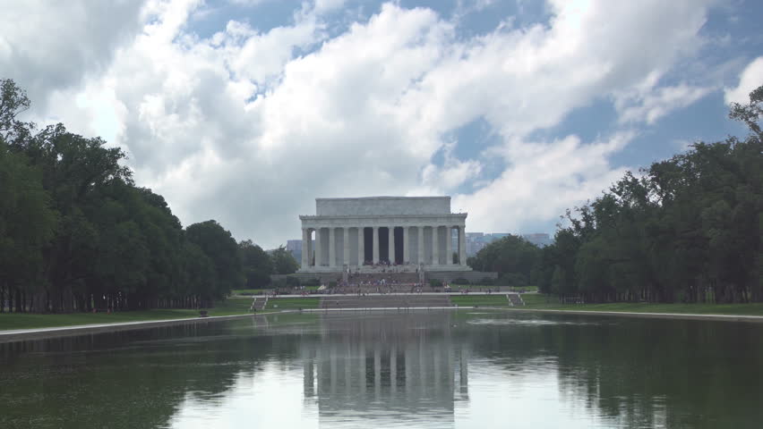 The Lincoln Memorial building and the reflecting pond shot midday against a fast passing cloud timelapse, unrecognizable tourists in the distance