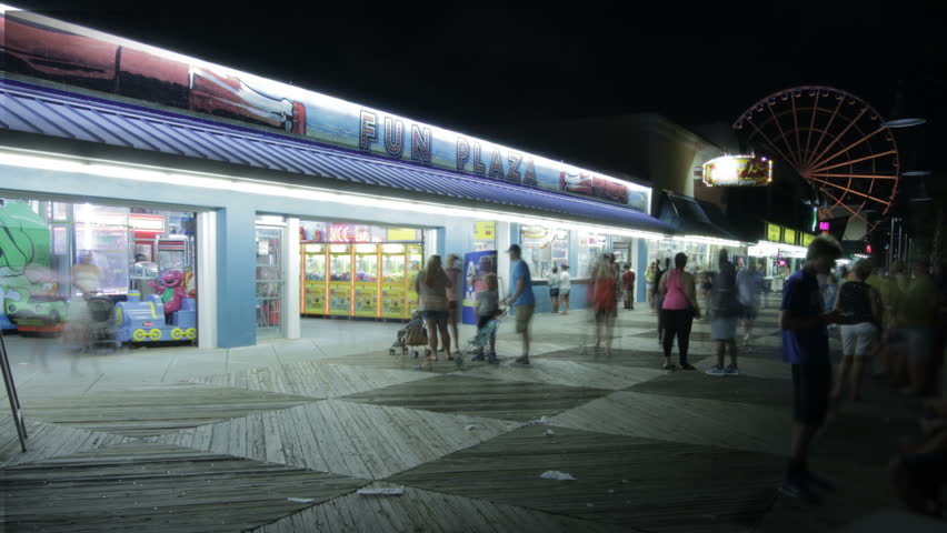 Time lapse of boardwalk in Myrtle Beach with people walking and ferris wheel in background at night.