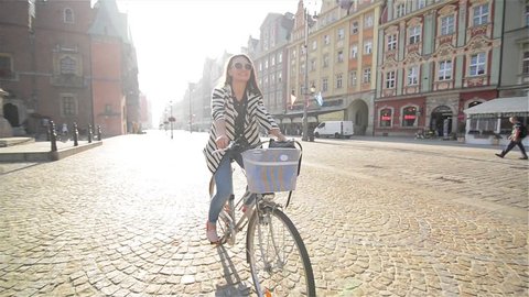 Beautiful young woman smiling while riding her bicycle on a sunny summer day through town in Slow Motion