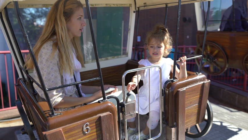 The toddler with her mom riding the carousel at the amusement Park.