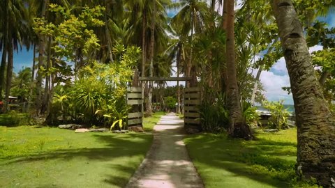 Camera moving through rustic gates to village with palm trees on lawn grass, Philippines