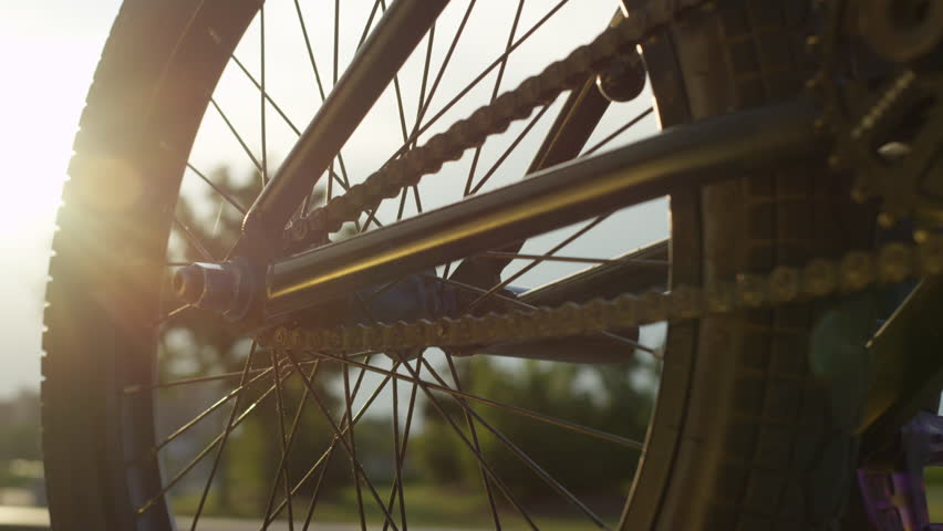 SLOW MOTION EXTREME CLOSE UP DOF: Details of a bmx bike equipment, biker spinning the wheel on summer evening. Sun shining through bmx bike wheel and chain, rider rides away on a street in sunny park | Shutterstock HD Video #19672975
