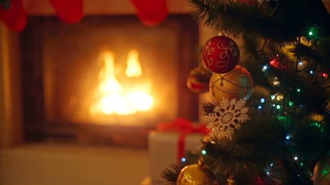Background with colorful baubles on Christmas tree next to burning fireplace at living room