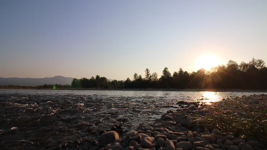 The flowing water of a mountain river bottled backlit setting sun. Video shot on the Canon 70D.