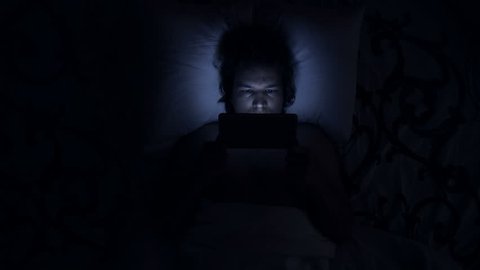 Man uses tablet computer in bed. Watching movies or going on social media, using a device before sleep with insomnia or sleeplessness. Causes are shining blue light or internet addiction.