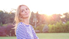 High quality 10bit footage of Happy Beautiful Young Woman Sitting on the Grass in City Park and Smiling at Sunset. Made from 14bit RAW.