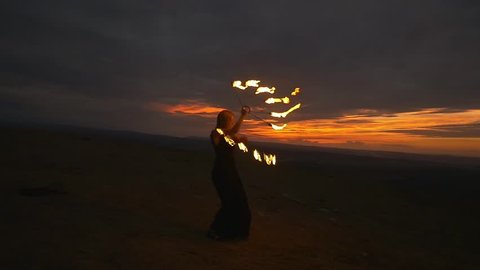 Woman with burning torches at the top of the mountain above the city at night. Actor does a fire performance outdoor on the top of the hill