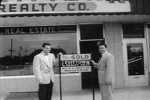 Real estate agents work in their office, and hammer a sold sign into a yard in Levittown, PA in the 1950s. (1950s)