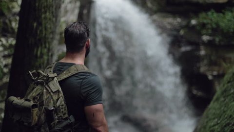 A male hiker watches a waterfall in slow motion.