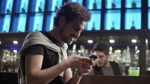 4K Young man sitting at a bar and sending message on the mobile phone with smile. Shot on RED EPIC Cinema Camera.
