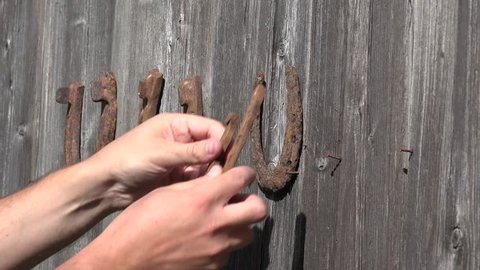 Country man hand hang old rusty horseshoes on old wooden door - symbol of luck. 4K